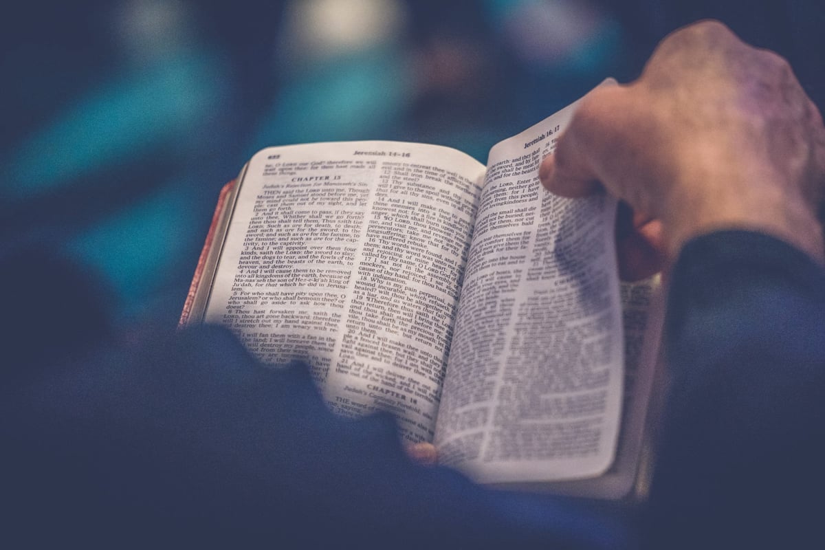 Person holding and reading an open Bible with blurred background, warm lighting illuminating the pages